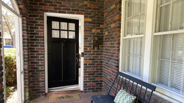 A brick exterior with a black door, a bench with a cushion, and a window with blinds. - Beautiful 1930s brick home in historic district. (Sumter)