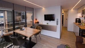 Eine moderne Küche mit Flachbildfernseher, einer Kaffeemaschine und einem Essbereich mit Holztisch und Stühlen.