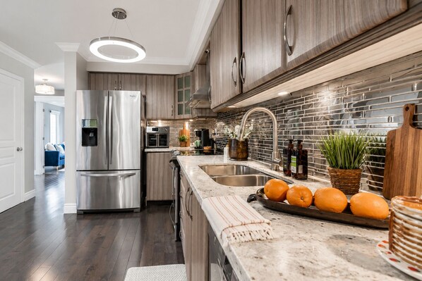 A modern kitchen with stainless steel appliances, a marble countertop, and a brick backsplash.