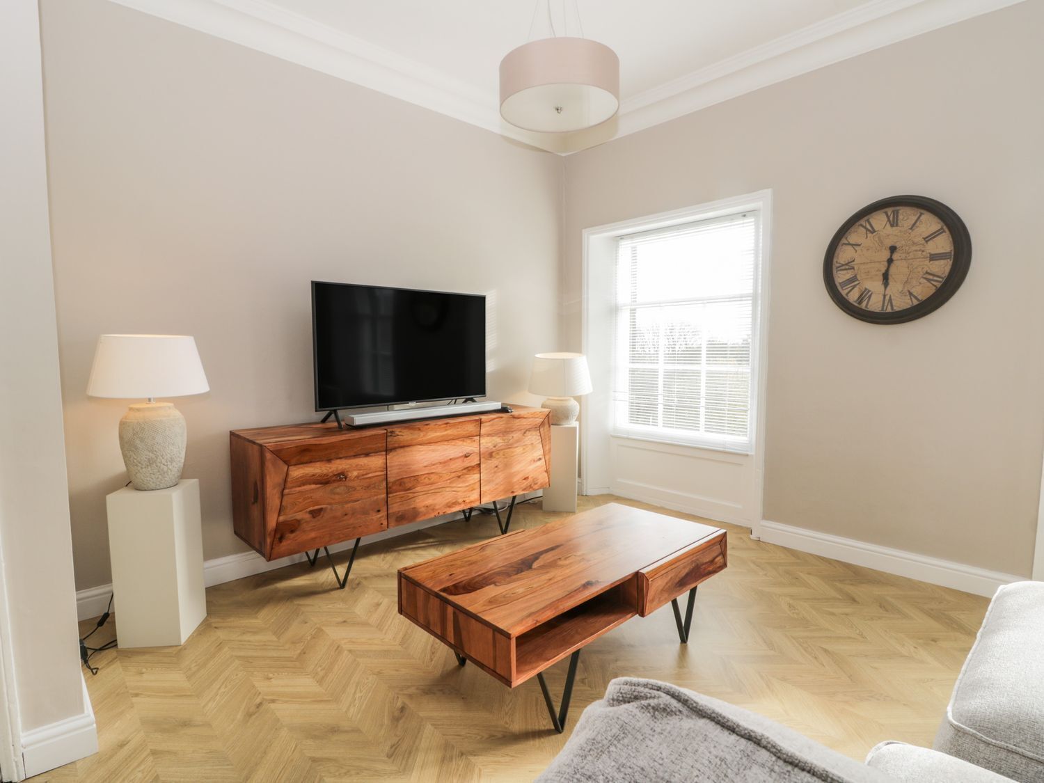 A modern living room with a television on a wooden cabinet, a coffee table, and a wall clock.