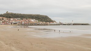A beach with a town in the background, a lighthouse, and a hill with a tower. - 7a Belvoir Terrace (Scarborough)
