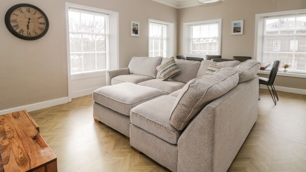 A living room with a sectional sofa, a wooden coffee table, and a wall clock. - 7a Belvoir Terrace (Scarborough)