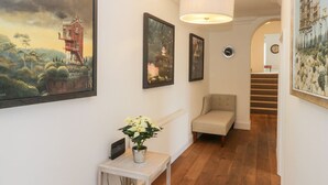 A hallway with framed paintings, a potted plant, a chair, and a staircase leading to another room. - 7a Belvoir Terrace (Scarborough)