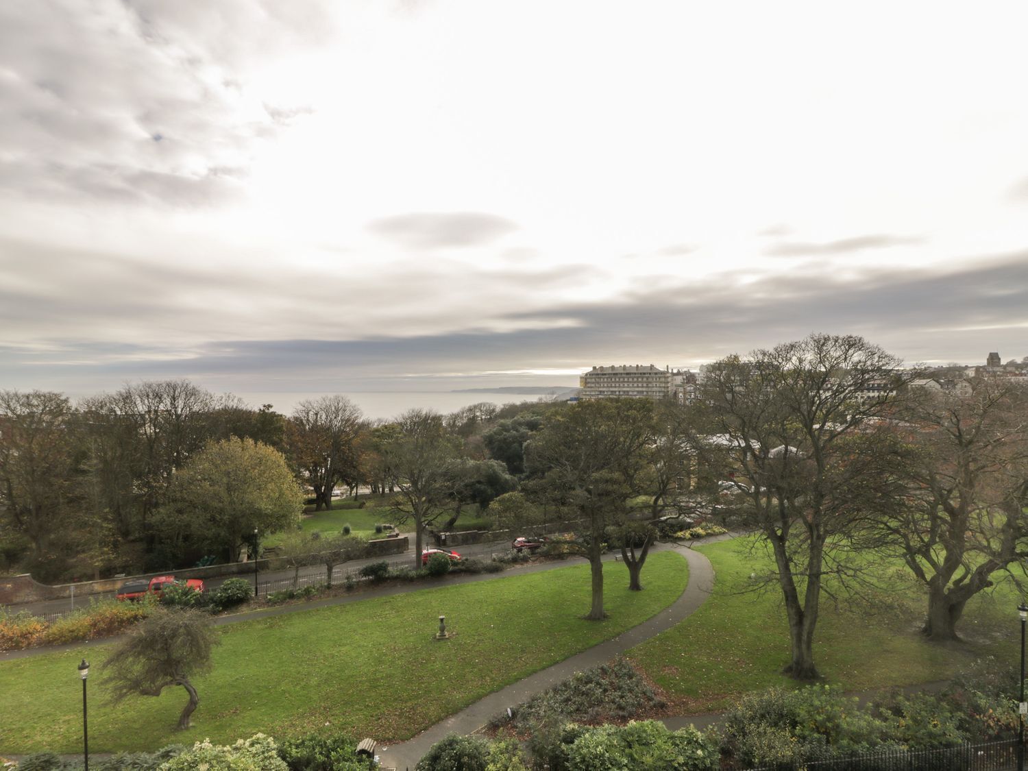 A park with a curved pathway, trees, and a distant building.