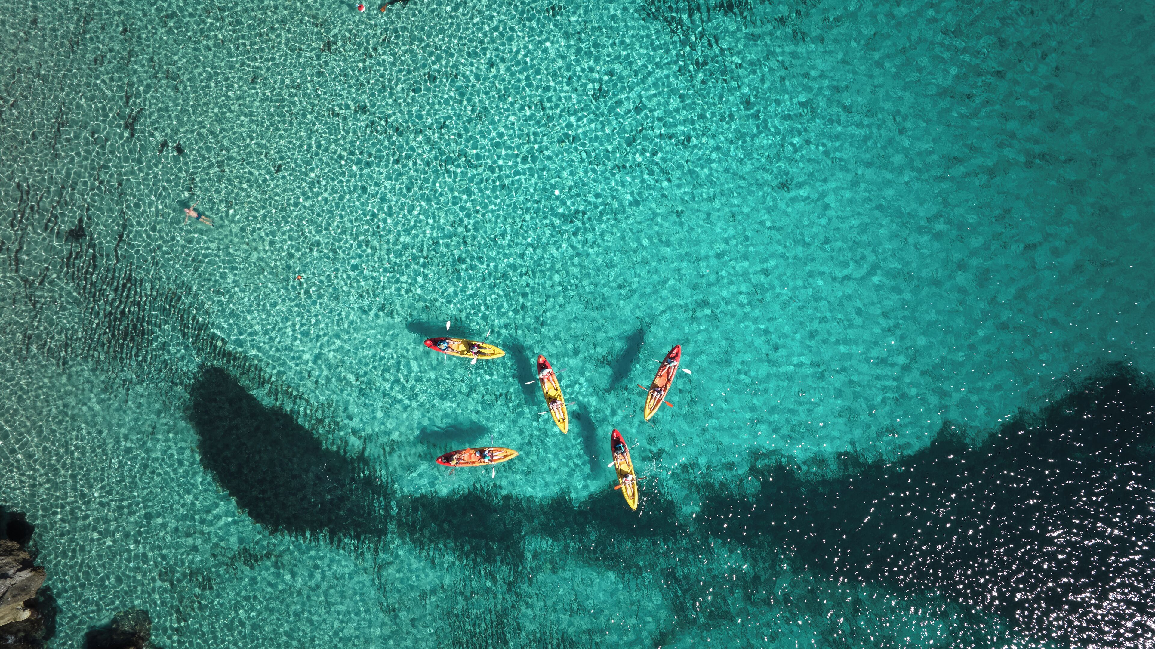 A clear turquoise water body with kayaks and a person paddling.