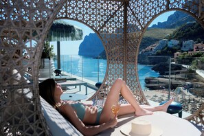 A woman relaxing on a lounge chair with a glass of wine, overlooking a coastal view with a pool and a mountainous backdrop. - Hotel El Vicenç de la Mar - Adults Only (+12) (Pollenca)