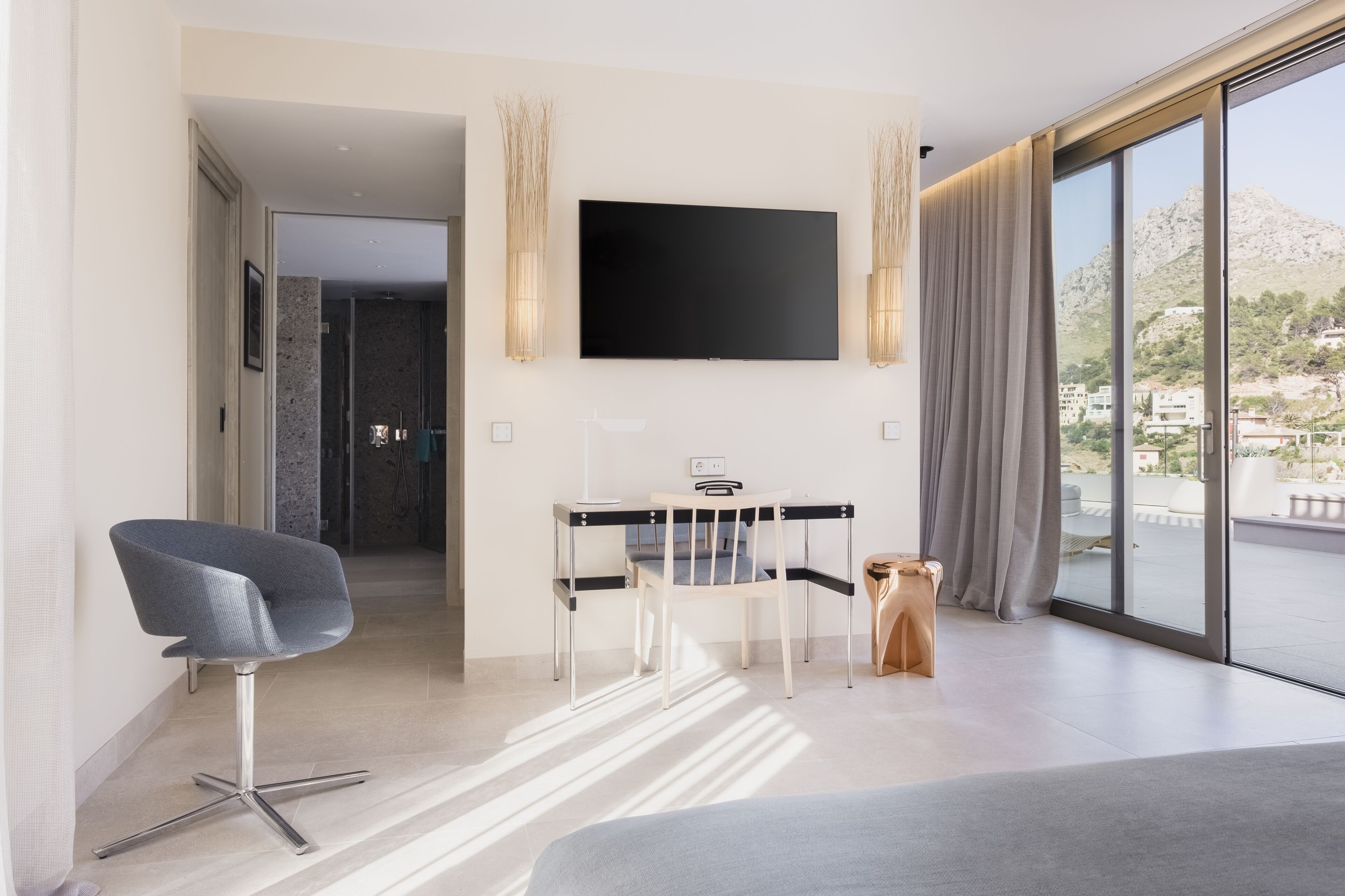 Une chambre d’hôtel moderne dotée d’un grand lit, d’un bureau avec une chaise, d’un téléviseur à écran plat fixé au mur et d’une grande fenêtre offrant une vue sur les montagnes.
