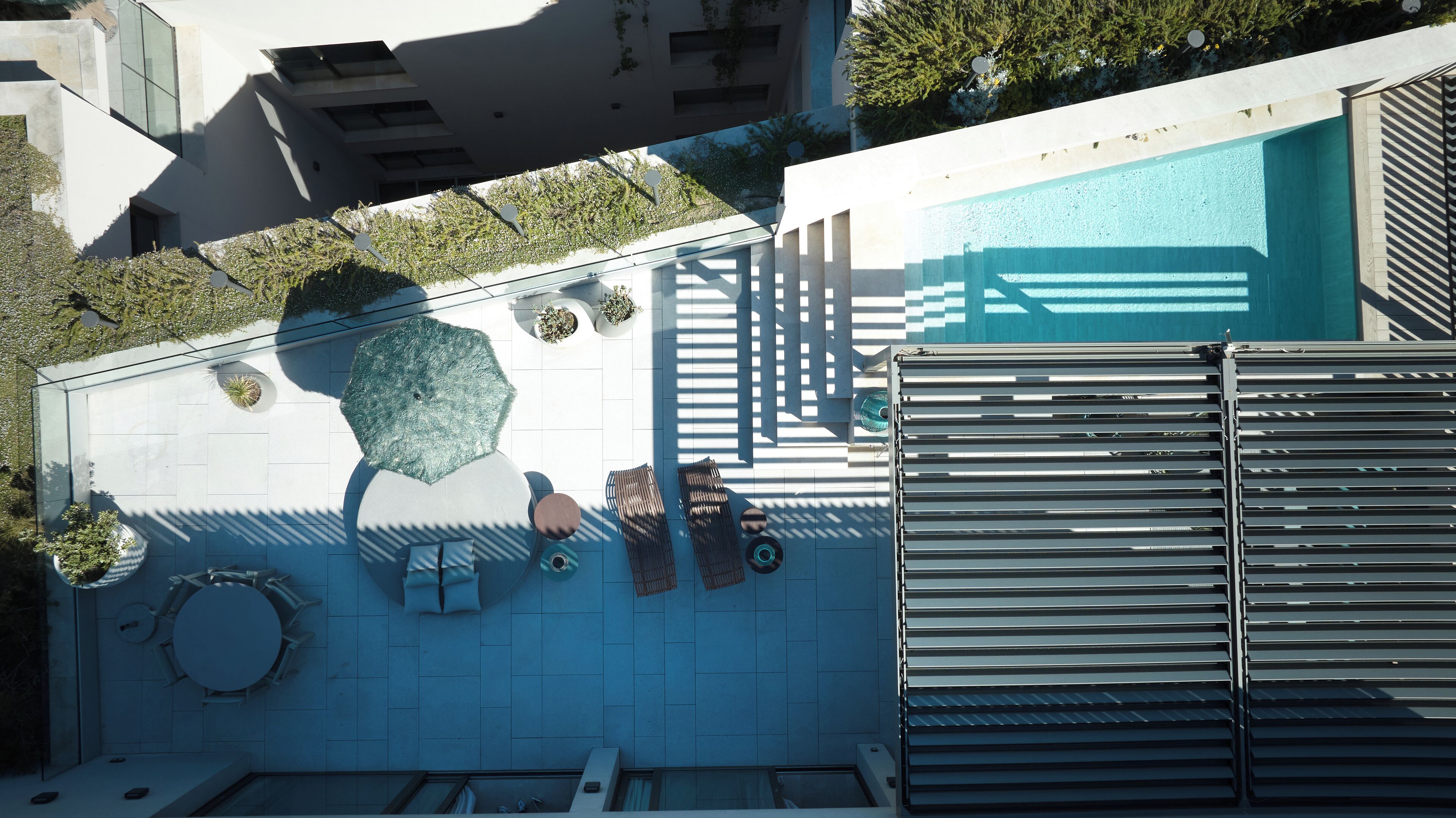 Vista aérea de una zona de piscina en la azotea con un diseño moderno, que incluye una sombrilla de cristal, sillones de descanso y una reja metálica.