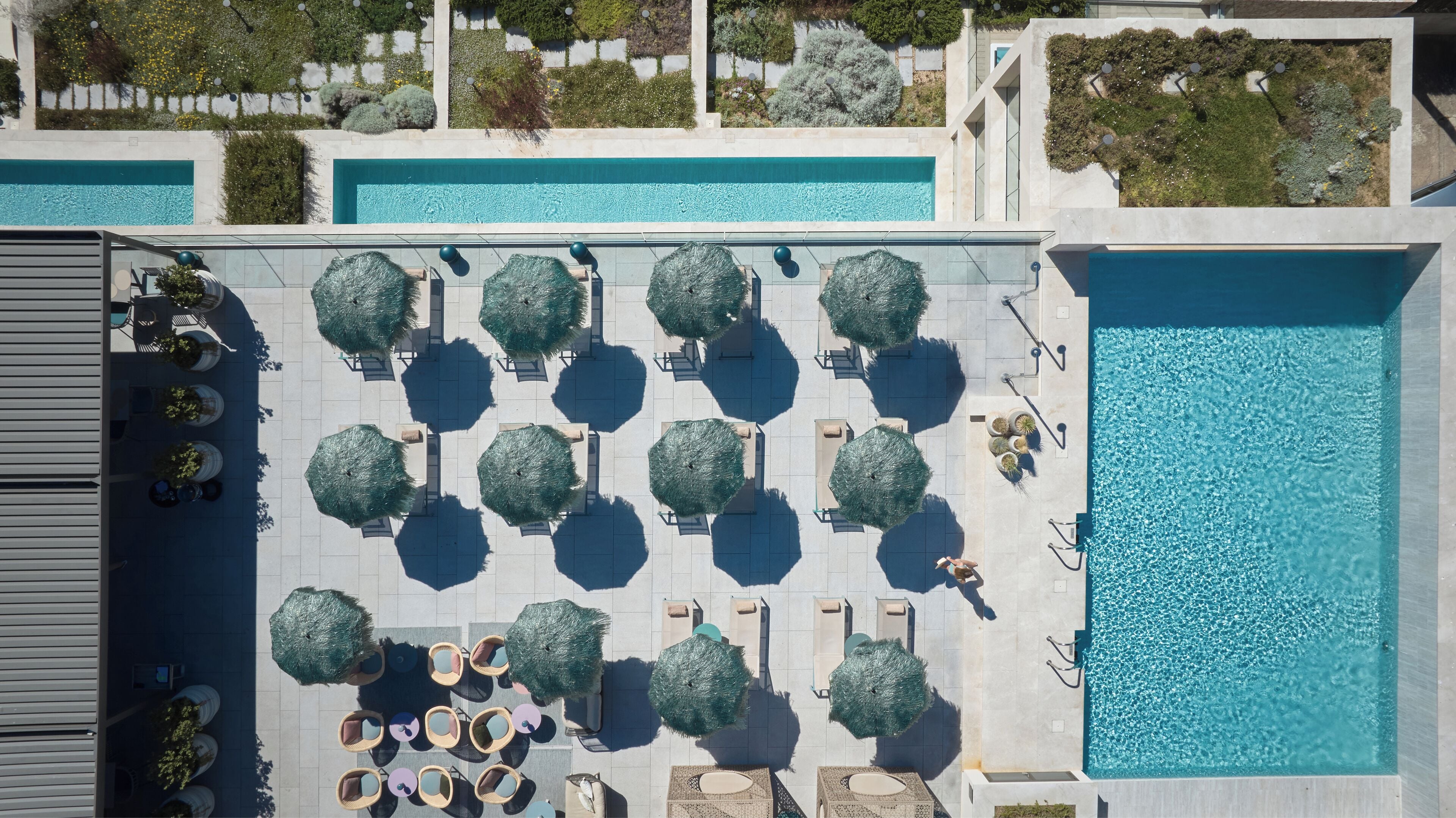 An aerial view of a rooftop pool area with multiple seating areas, umbrellas, and a large swimming pool.