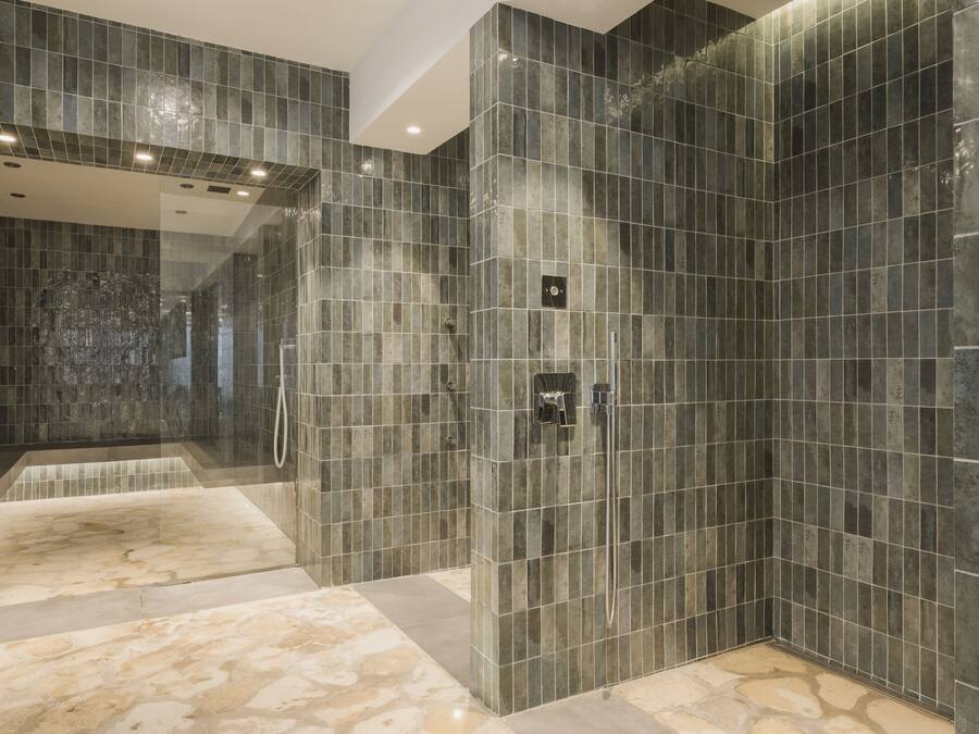 Un baño moderno con paredes de azulejos oscuros, cabina de ducha con mampara de vidrio y suelo de mármol.