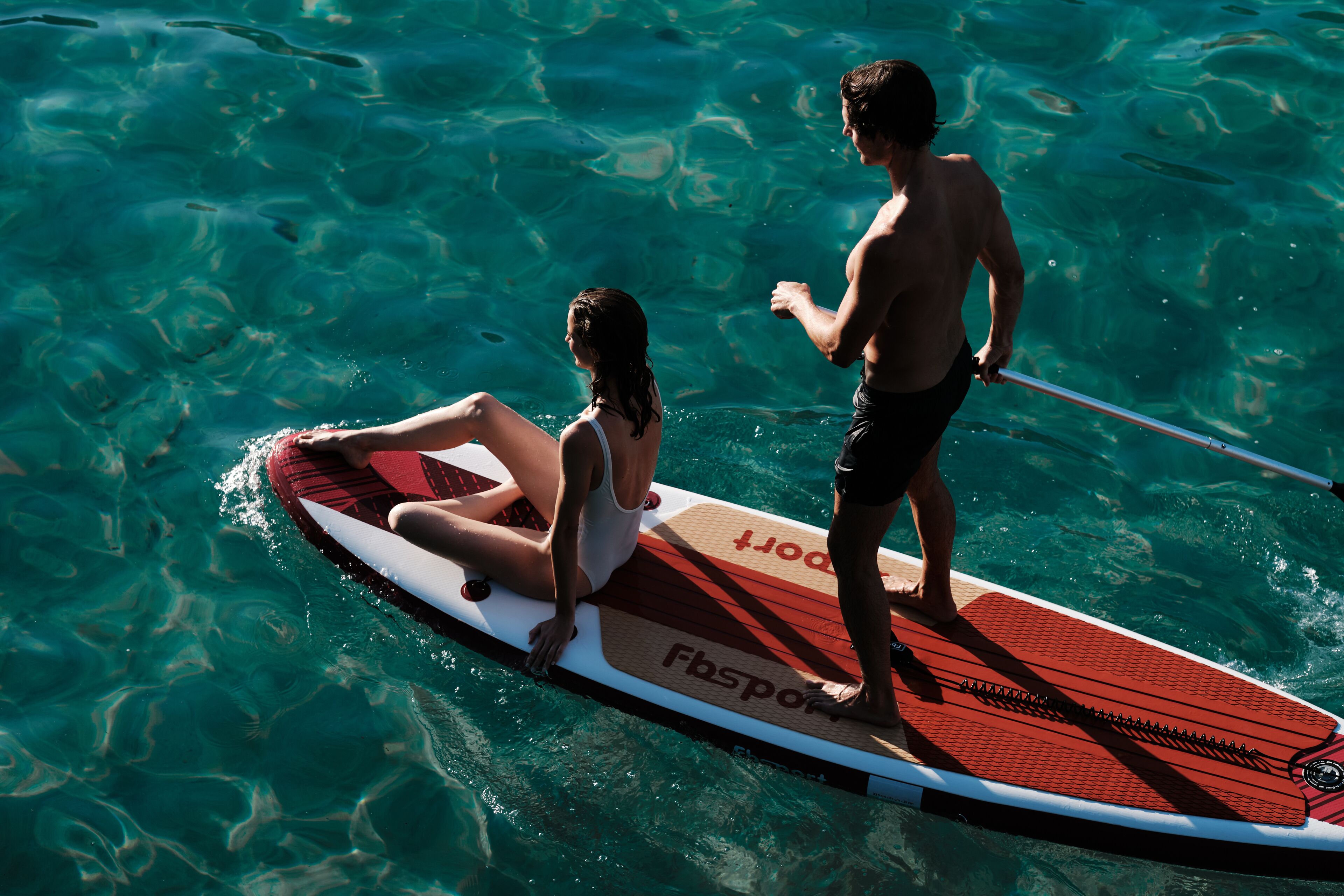 Eine Person steht auf einem Stand-Up-Paddleboard in klarem Wasser.