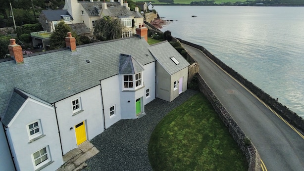 Un bâtiment situé sur la côte, avec une allée pavée, une porte jaune et une vue sur la mer.