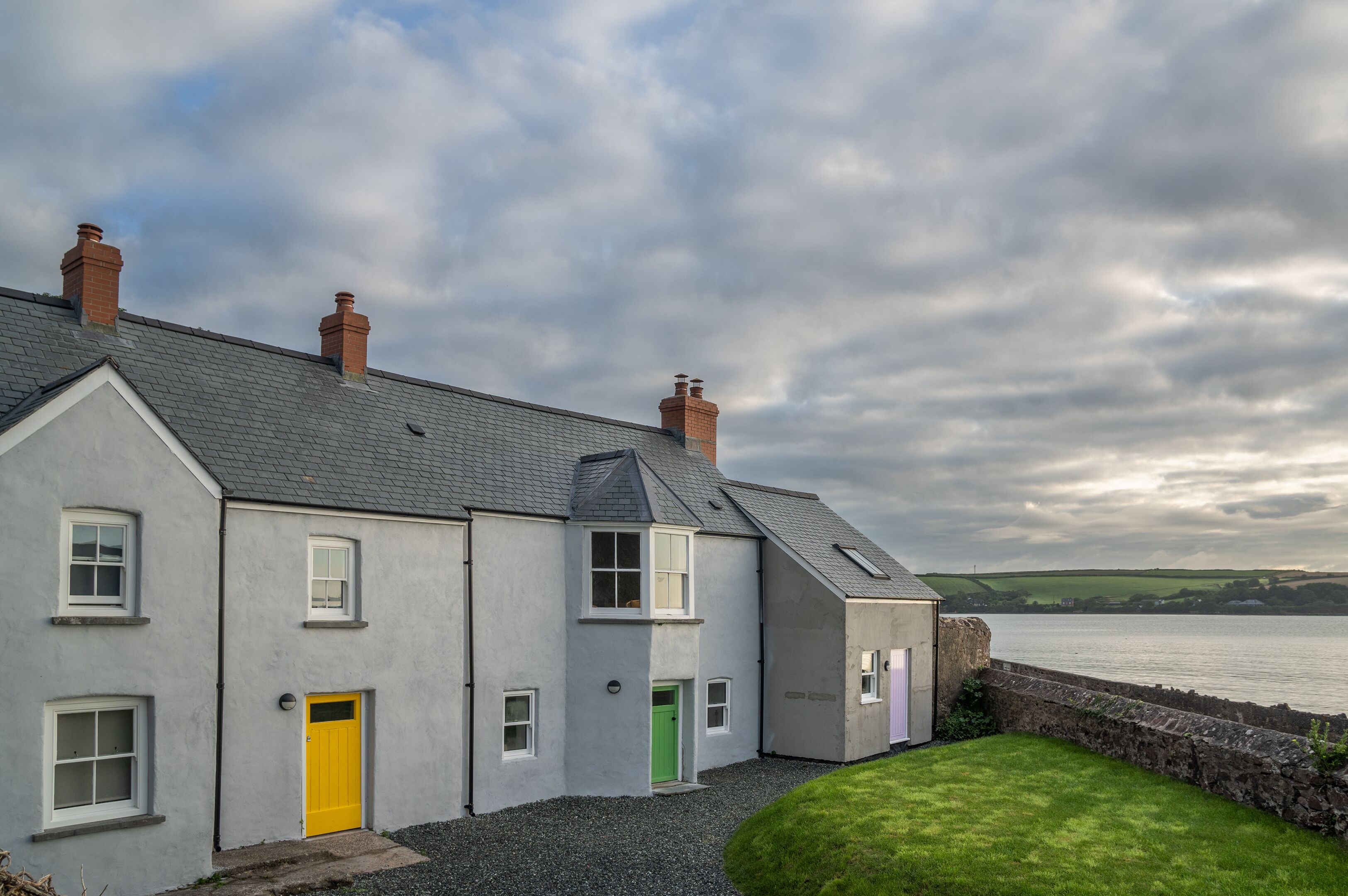 A coastal house with a grey exterior, multiple chimneys, and a stone wall.