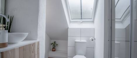 A modern bathroom with a skylight, white fixtures, a wooden vanity, and a small potted plant.