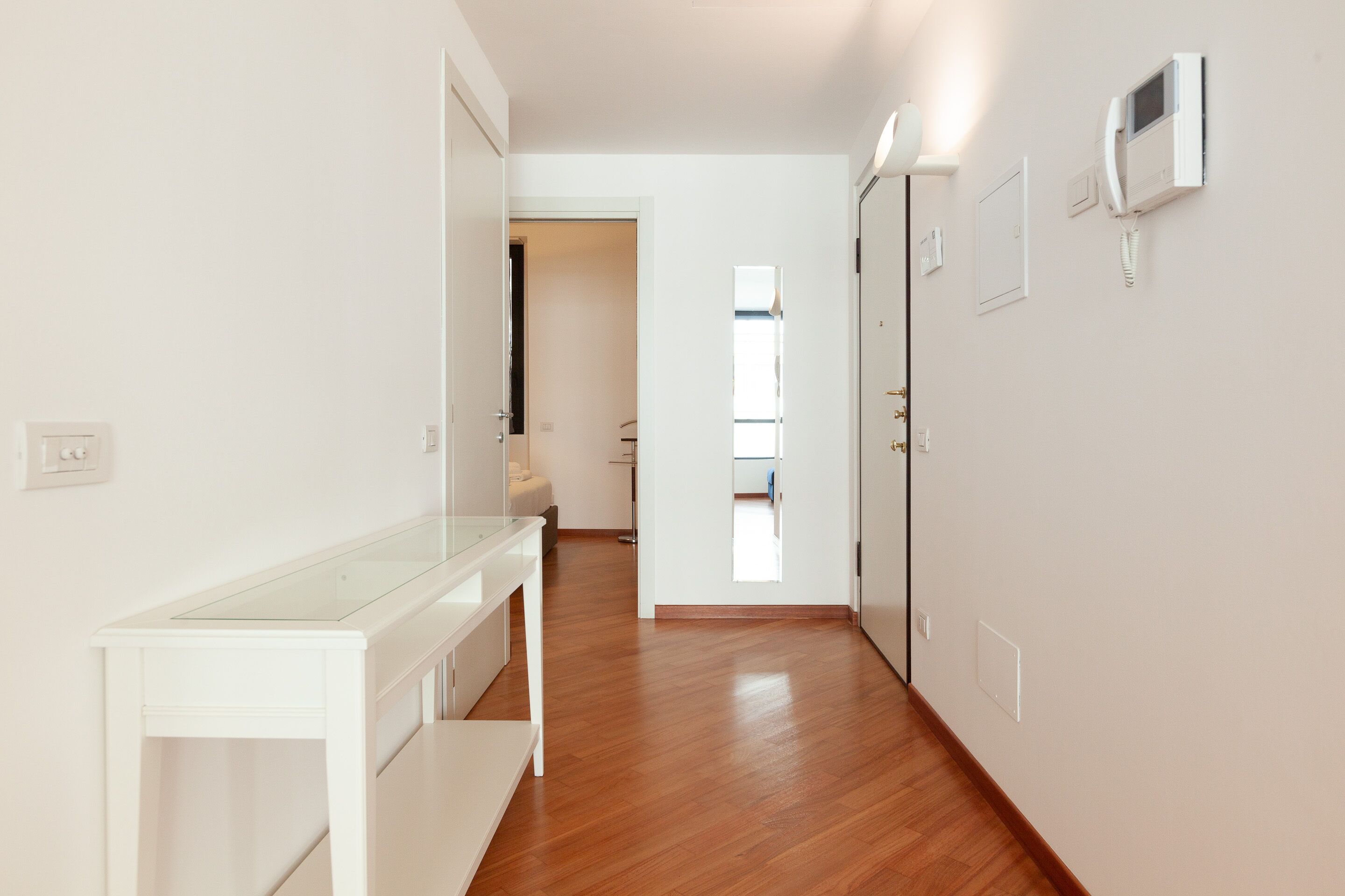 A hallway with a white console table, wooden flooring, and a door leading to another room.