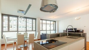 A modern kitchen with a central island, a dining area with a glass table, and large windows offering views of the city. - easyhomes - Madonnina view (Milan)