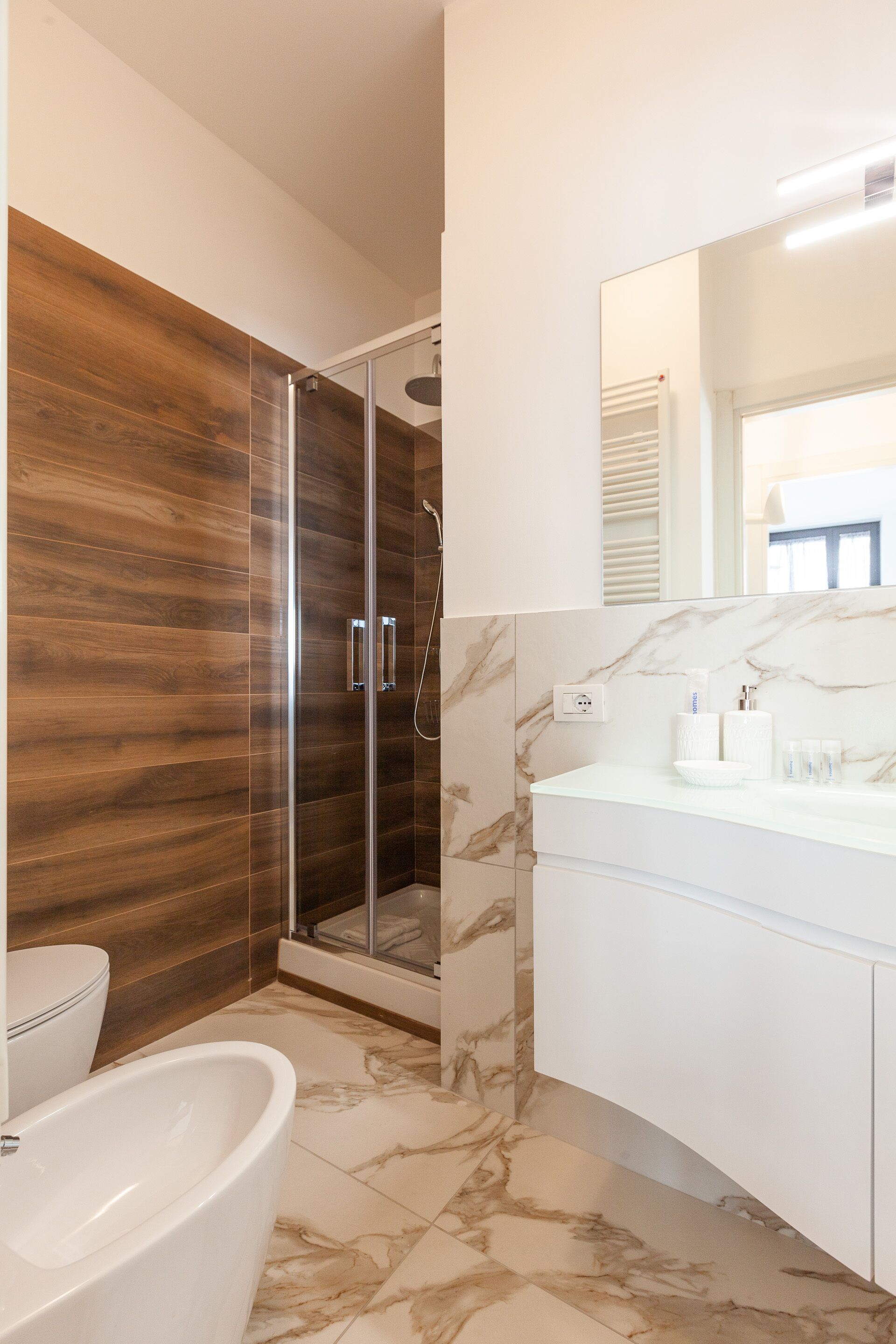 Un baño moderno con ducha envuelta en vidrio, una bañera blanca y suelo de mármol.