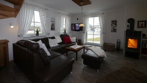 Una sala de estar moderna con chimenea, sofás de cuero, televisor y un amplio ventanal.