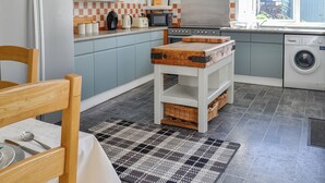 Una cocina compacta con armarios azul claro, una isla central con cestas, una lavadora y un ventanal con vistas al exterior.