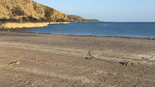 Una playa con un acantilado rocoso y un mar tranquilo.