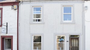 Un edificio con fachada blanca, varias ventanas y una puerta con placa numérica.