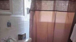 Pieni kylpyhuone, jossa on wc, pesuallas ja suihkuverho.
