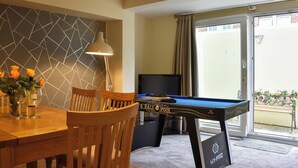 Une pièce avec une table de billard, une table à manger avec des chaises, un téléviseur et une vue sur l’extérieur.