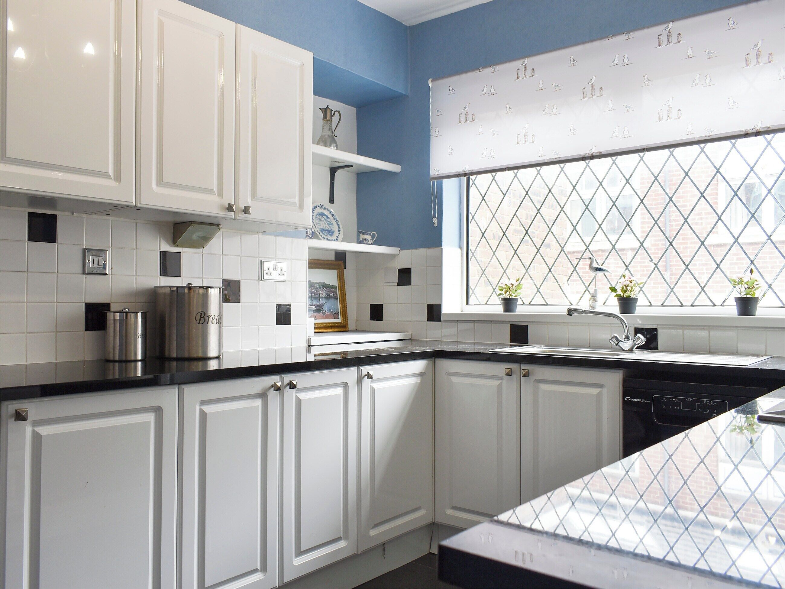 A kitchen with white cabinets, a black countertop, a window with a diamond-patterned blind, and a sink.