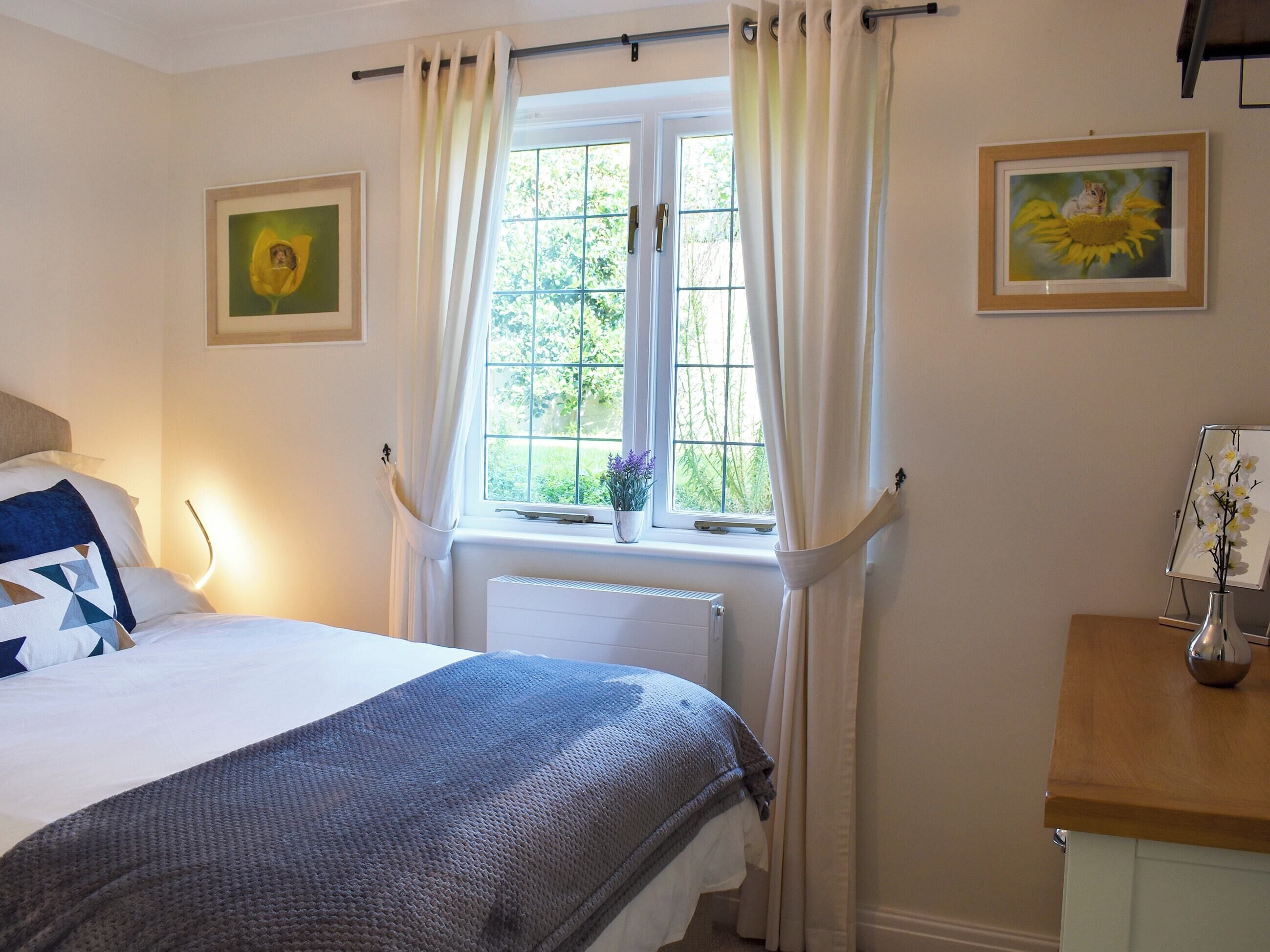 Une chambre à coucher avec un lit, une fenêtre avec des rideaux, un radiateur et deux tableaux encadrés accrochés au mur.