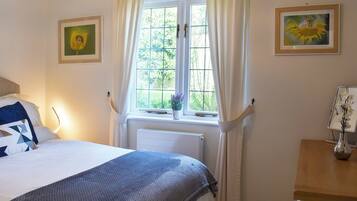Une chambre à coucher avec un lit, une fenêtre avec des rideaux, un radiateur et deux tableaux encadrés accrochés au mur.
