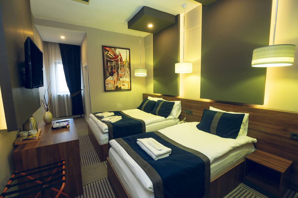 Une chambre d’hôtel avec deux lits, un bureau avec une chaise, une télévision et un tableau au mur.