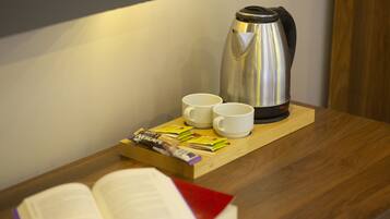A wooden table with a stainless steel coffee maker, two white cups, and a tray with tea packets and a book.