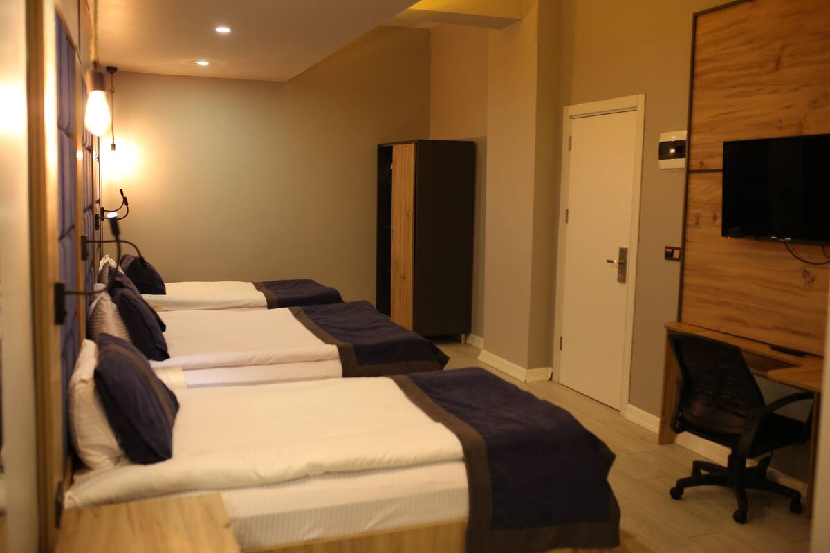 Une chambre d’hôtel avec trois lits, un téléviseur fixé au mur, un bureau avec une chaise et une armoire.