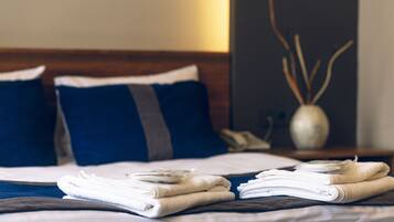 Una cama bien hecha con toallas dobladas y un florero con ramas decorativas sobre una mesita de noche.