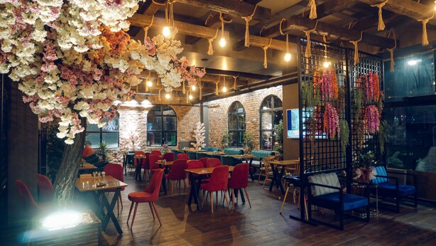 L’intérieur d’un restaurant avec un plancher en bois, des chaises rouges et des décorations florales suspendues.