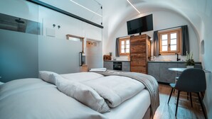 Ein modernes Hotelzimmer mit einem großen Bett, einer kleinen Küchenzeile, einem Essbereich und einem an der Wand befestigten Fernseher.