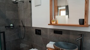 Ein modernes Badezimmer mit einer Duschkabine aus Glas, einer weißen Toilette, einem Holzwaschtisch mit Steinbecken und einem Spiegel über dem Waschtisch.