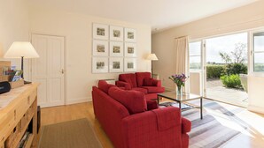 A living room with a red sofa set, a coffee table, and a lamp. There are framed pictures on the wall and a view of the garden through the window.