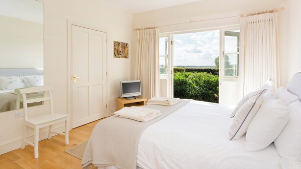 A bedroom with a bed, a TV, a chair, and a window with curtains.