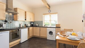 A modern kitchen with wooden cabinets, a built-in oven, a dishwasher, and a window with blinds.