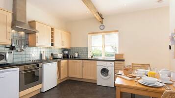 A modern kitchen with wooden cabinets, a built-in oven, a dishwasher, and a window with blinds.