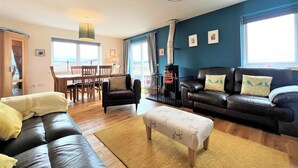 Ein Wohnzimmer mit einer Couch, einem Hocker und einem Essbereich mit Stühlen und einem Tisch.