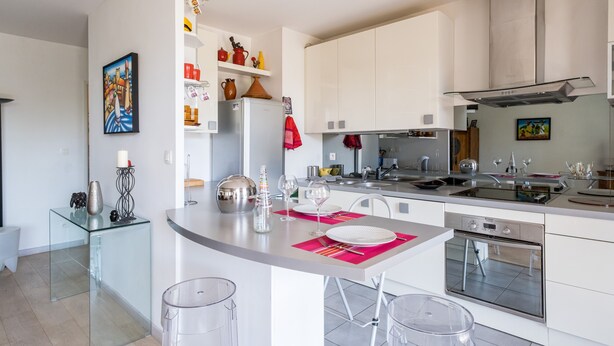 Una cucina moderna con mobili bianchi, un piano cottura in acciaio inossidabile e un tavolo da pranzo in vetro con sedie trasparenti.