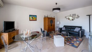 Un soggiorno moderno con un tavolo da pranzo in vetro, un divano in pelle nera, un armadietto in legno e un tappeto colorato.