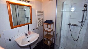 Une salle de bain équipée d’un lavabo, d’un miroir, d’un porte-serviettes, d’une douche et d’un radiateur.