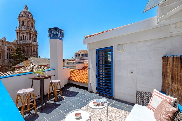 A rooftop terrace with a table, chairs, and a sofa, overlooking a historic building with a dome.