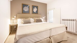 A neatly arranged bedroom with a large bed, two bedside lamps, and framed artwork on the wall.
