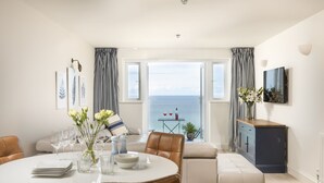 Een moderne woonkamer met een eethoek, een bank, een kast en uitzicht op zee.