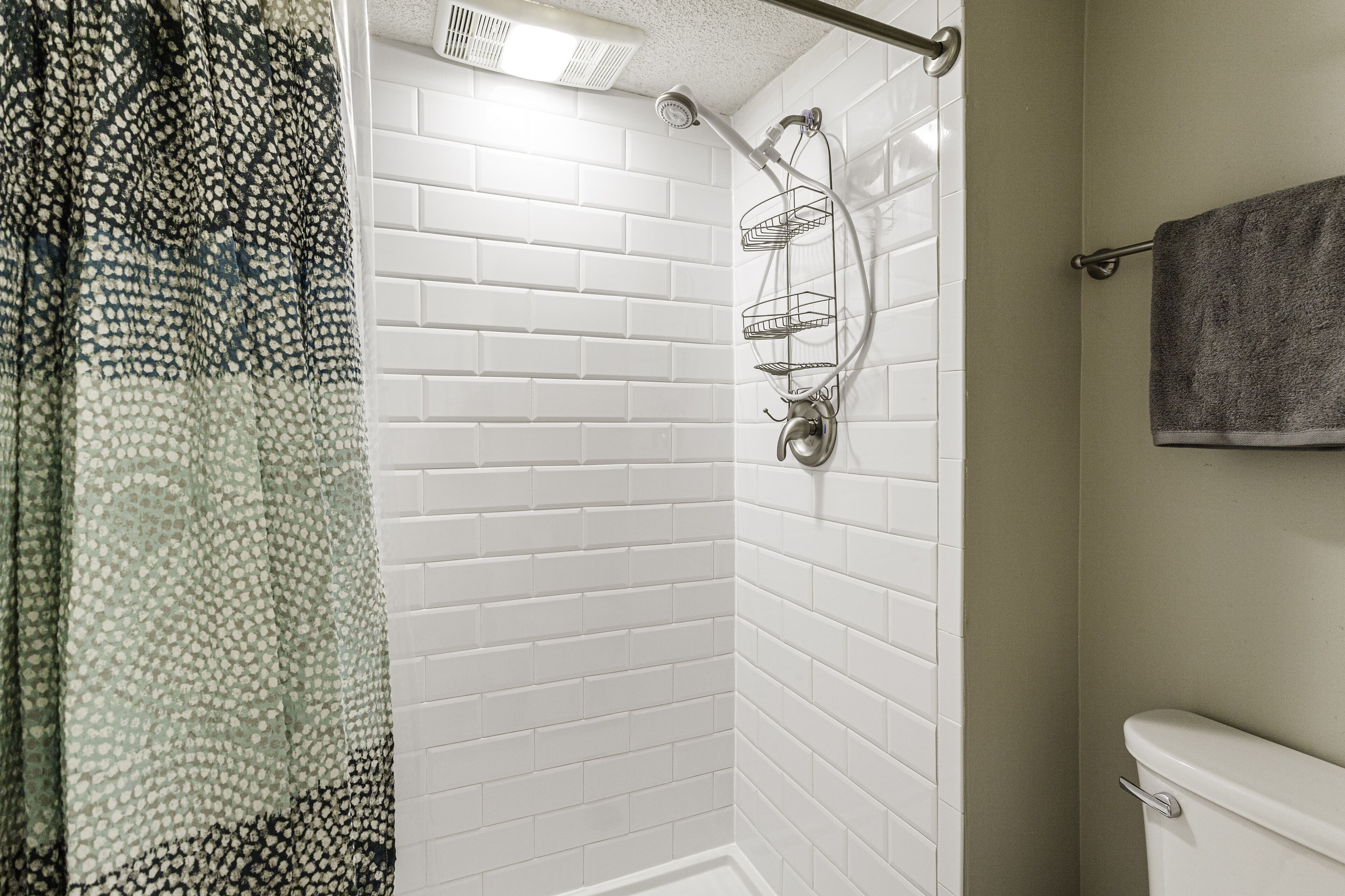 Un área de ducha con paredes de azulejos blancos, un cabezal de ducha y un perchero para toallas.