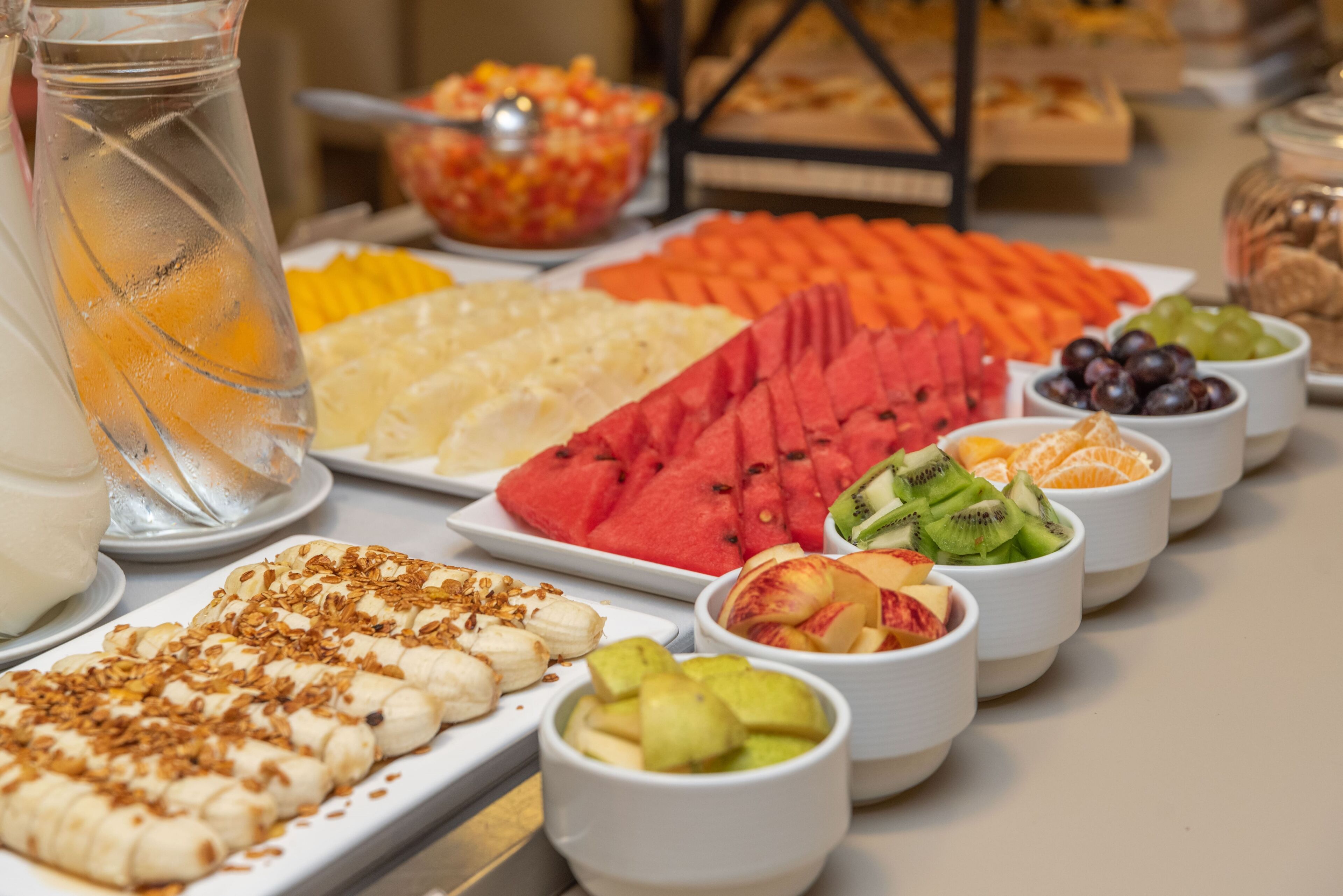 A buffet table with various fruits and a pitcher of iced tea.